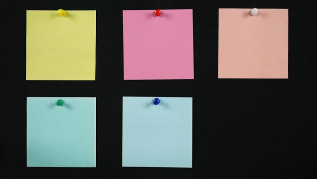 Blank paper sticky notes appear on a black board. Stop motion animation of the appearance of color note stickers