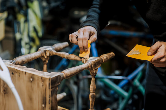 A man is a professional carpenter, a woodworker, applying putty and cement to a wooden chair in the workshop. Photography, handmade concept. - Powered by Adobe