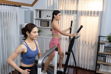 Energetic and strong athletic asian woman running on elliptical running machine at home with...