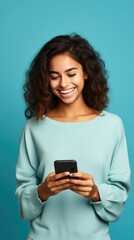Fototapeta premium Radiant woman with dark skin in a blue shirt, beaming at her phone against a vivid blue backdrop, exuding joy