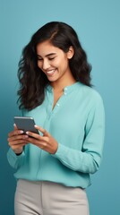 Fototapeta premium Radiant woman with dark skin in a blue shirt, beaming at her phone against a vivid blue backdrop, exuding joy