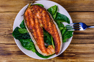 Plate with roasted salmon steak and spinach leaves on a wooden table