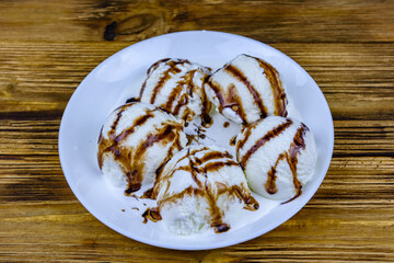 Plate with ice cream balls and chocolate topping on a wooden table