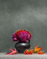 Still life with flowers and berries on a dark background. Pink, red dahlias in a gray vase, orange...