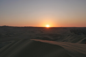 Last rays of orange sunet reflecting on a dune in the foreground.  Location:  Huacachina, Peru
