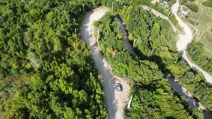 Aerial view of a curved countryside road with a car surrounded by green vegetation