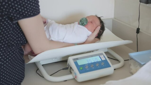 Newborn baby wrapped in blanket gently transferred for weighing to baby scales in hospital nursery. Lady ensuring baby weight accurately determined