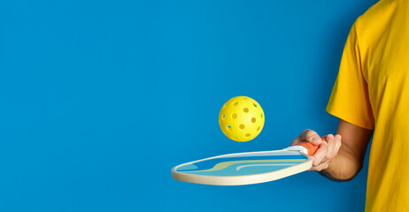 hand with paddle and yellow pickleball ball on blue background