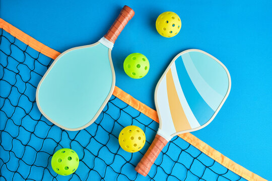 two paddles and four pickleball balls on top of a net on blue background