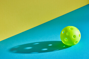 green pickleball ball with shadow on a blue surface with a yellow wall next to it