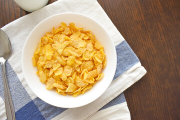 Cornflakes in a white bowl, a spoon and a bottle of milk on wood table. Copy space is on  the right. Healthy breakfast. Dietary food concept. 