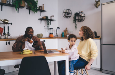 Positive diverse couple with daughter eating breakfast while spending time together at dining table