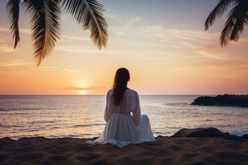 Lovely graceful lady sit by beach at sunset with beautiful seascape. Summer tropical vacation concept.