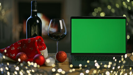 Glass and bottle of red wine with laptop computer on table in Christmas decorated room. Christmas...