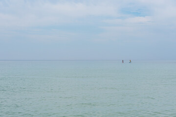 Fototapeta premium sea and blue sky of identical hue, on the right side two people practicing padlle. Atlantic ocean on the Algarve coast of Portugal