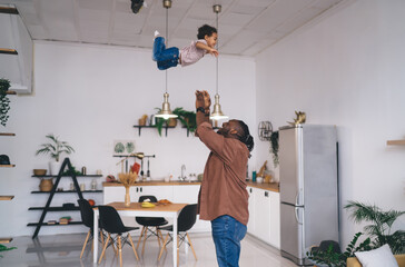 Happy father throwing cute kid while playing in modern apartment