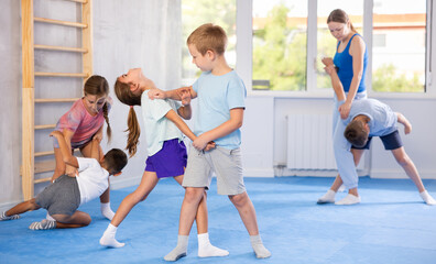 Obraz premium Children boy and girl partner in sparring practice technique practicing basic attacking movements and maneuvers. Class self-defense training in presence of experienced instructor