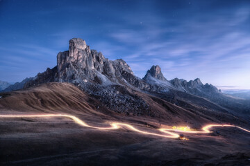 Car light trails on mountain road and high rocks at night in autumn in Passo Giau, Dolomites,...