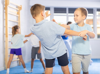 Kids in sportswear exercising self-protection techniques in pair during class at gym