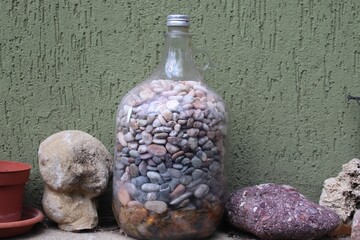 Closeup of a composition of pebbles in a jar with bigger rocks against a green wall