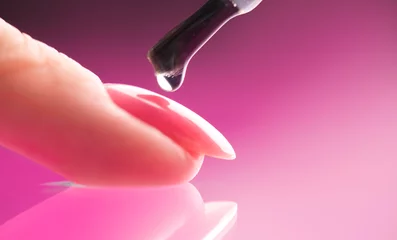 Applying Nail polish, pink shellac UV gel, varnish, manicure process concept in beauty salon. Transparent top coat drop on brush. Over pink background. Application of nail polish