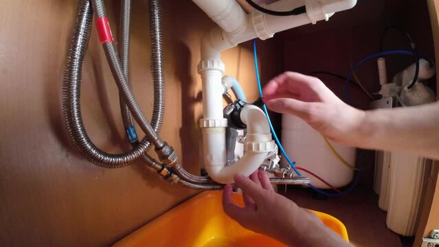 A man is repairing plumbing in the kitchen under the sink.