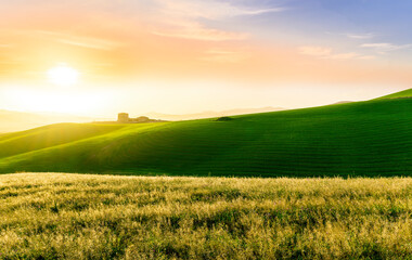 countryside sunset in green hills of spring fields with old castle farm and mountains on background of evening landscape