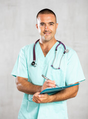 Portrait of male doctor in medical gown with stethoscope making notes in the patient medical history