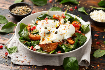 Roasted butternut squash salad served with poached eggs, spinach, nuts and pomegranate seeds
