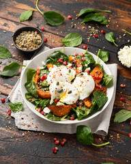 Roasted butternut squash salad served with poached eggs, spinach, nuts and pomegranate seeds - obrazy, fototapety, plakaty
