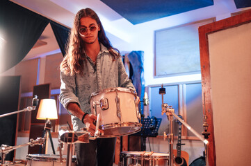 Drummer setting up a tom onto his drum set in a music studio.