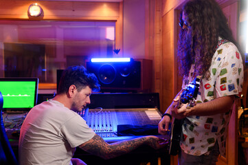 Music producer setting up a guitar for male guitar player in a music studio.