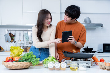 Happy Family portrait of loving young asian of having fun standing a cheerful preparing food See in the tablet and enjoy cook cooking meat, bread while standing on a kitchen Condo life or home