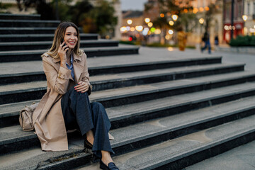 Stylish female sitting on a stairs in the city streets and using a mobile phone