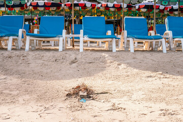 Beach workers swept garbage by broom on sandy beach in front of plastic chairs. Front view