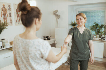 smiling therapist woman in massage cabinet shaking hands