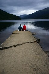 Back shot of elderly couple sitting on a shore of lake on stone pier