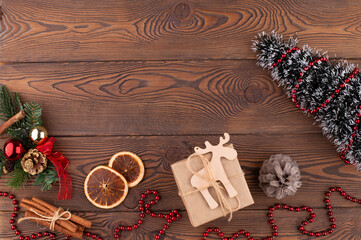 Christmas holiday background with wooden deer, tree decorated with pine cone, beads and gifts wrapped in craft paper, dried oranges on rustic wooden background, flat lay, copy space.