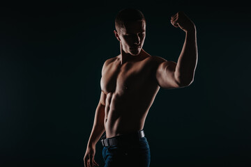 Fototapeta na wymiar Muscular and good-looking man standing in a dark room and flexing his bicep
