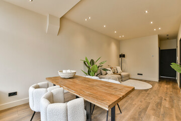 a living room with wood flooring and white walls, there is a large wooden dining table in the center of the room