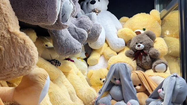 Many teddy bears of large and small sizes lie in a pile in the window of a toy store. A large selection of soft toys on store shelves. Teddy bear