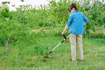 Woman mowing grass with cordless trimmer in garden