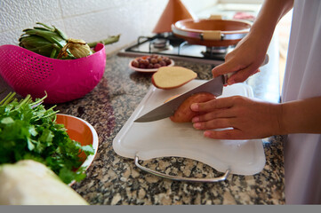 Obraz na płótnie Canvas Closeup view woman hands using kitchen knife, chopping organic potato on a cutting board, cooking dinner at home kitchen