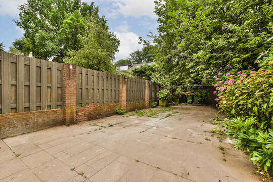 an empty backyard with brick walls and green trees in the background, on a sunny day stock photo - 1290891