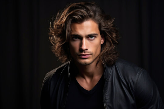Young man with long brown hair on dark studio background. Face of handsome male model wearing black casual jacket. Concept of style, fashion, beauty, guy portrait, stylish hairstyle