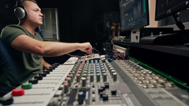 a focused male sound engineer wearing headphones sits at a mixing desk recording new track