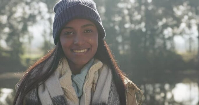 Nature, happy and face of a woman by a lake while on a winter weekend trip, holiday or adventure. Travel, freedom and portrait of an Indian female person with a smile in an outdoor forest or woods.