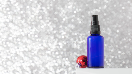 Dispenser with serum or oil for youthful skin on a silver background with a Christmas ball. Skin...