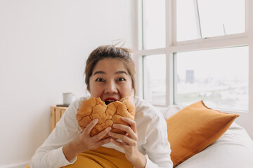 Asian woman eating bread and coffee breakfast sits on bean bag in living.