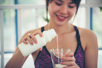 Women hands holding white glass of milk pouring from bottle. Asian women smile laugh look at camera...